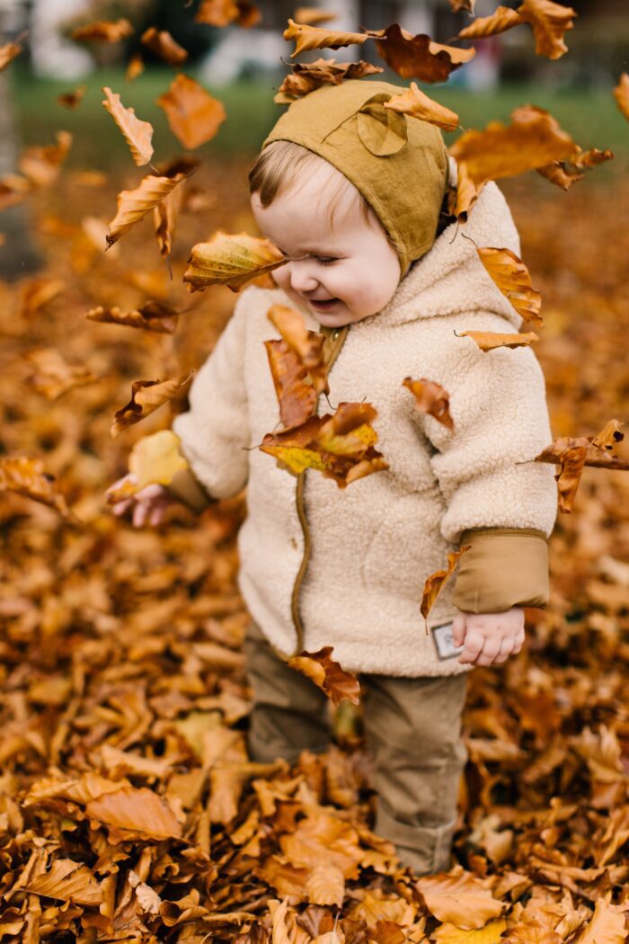 Child playing in autumnal leaves wearing cozy sustainable clothes.